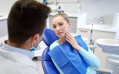 Woman with toothache in dentist's chair, dentist in foreground